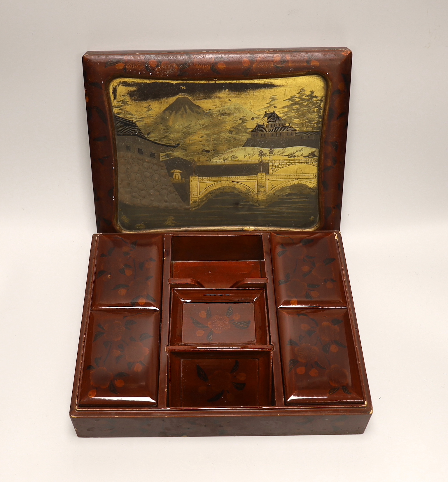 A Japanese lacquer games box, the cover having a central landscape painting together with a carved bamboo page turner, box 30 cm wide x 24 deep